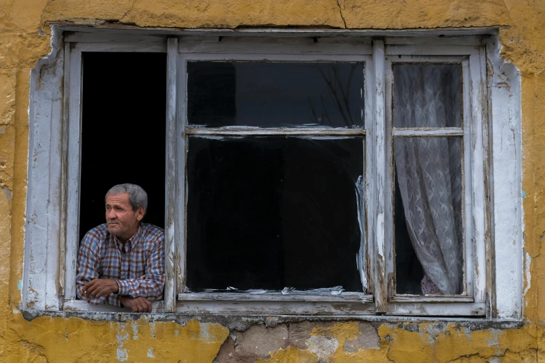 a man sitting in the window of an old, run down house