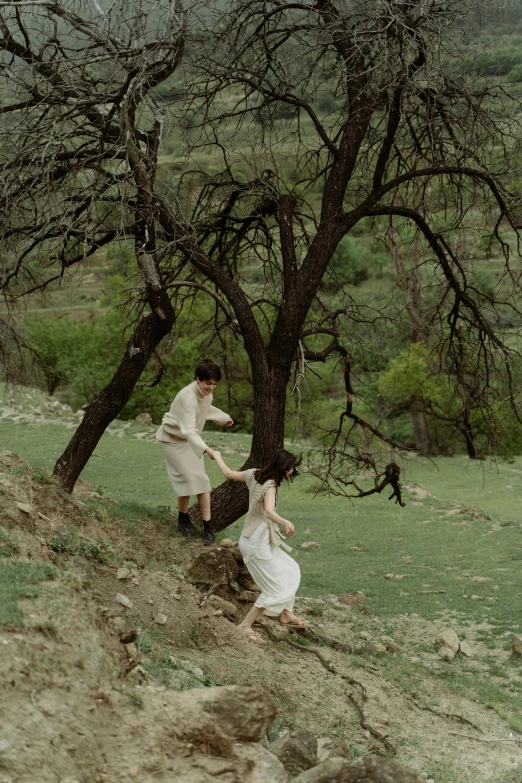 two people standing on top of a hill near a tree