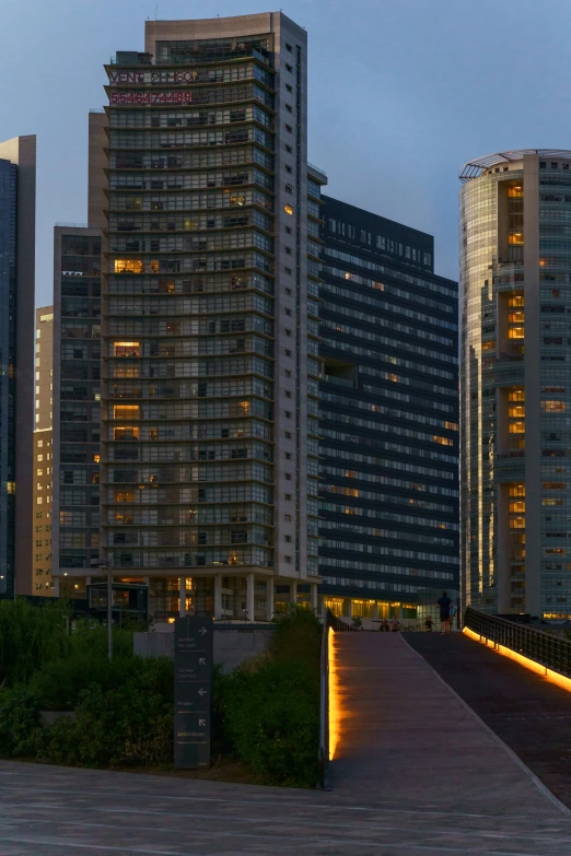 some tall buildings lights and walkway in the evening