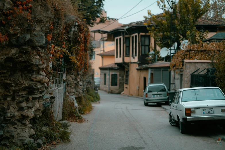 two cars parked in a street lined with stone walls