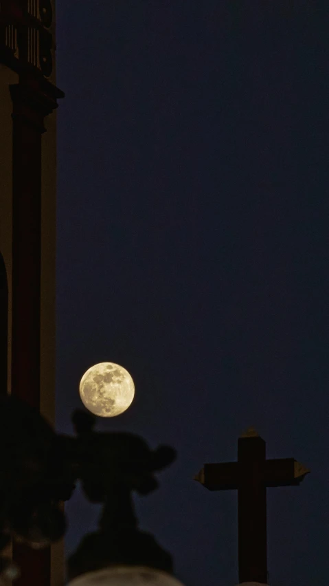 a view of a full moon through the skies of a cross