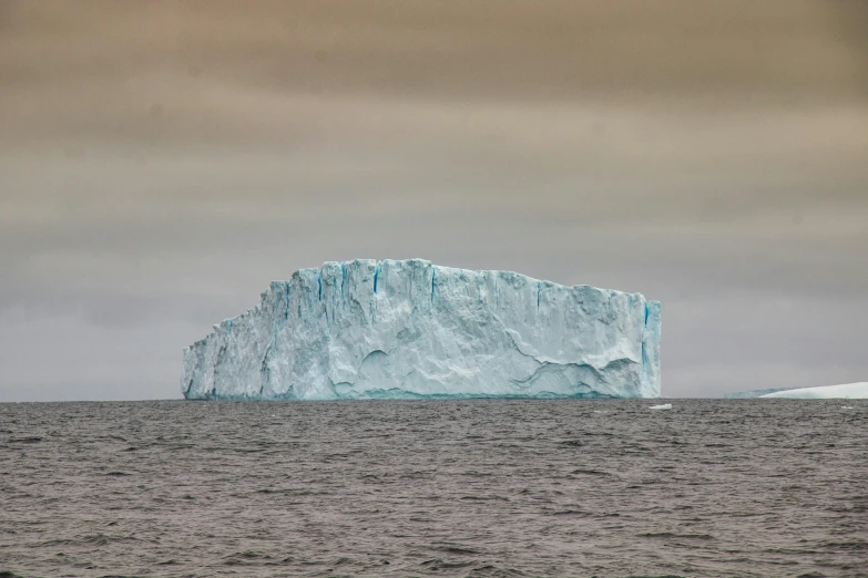 an iceberg floating on water under a cloudy sky