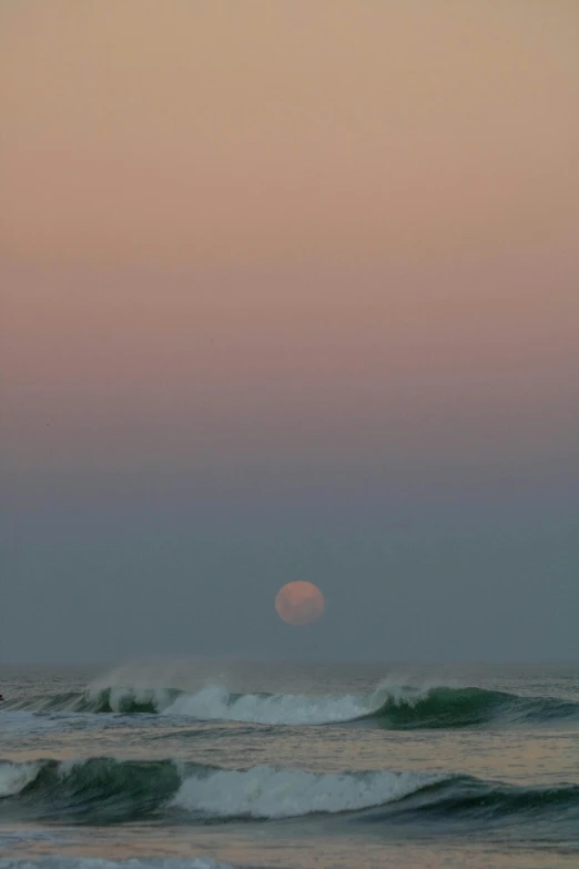 a surfer in the ocean at sunset with a pink sky