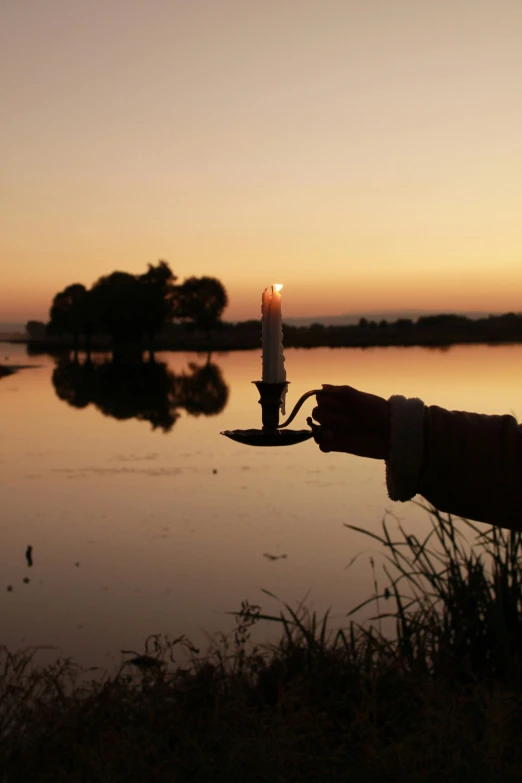 a hand holding a lighter next to a lake