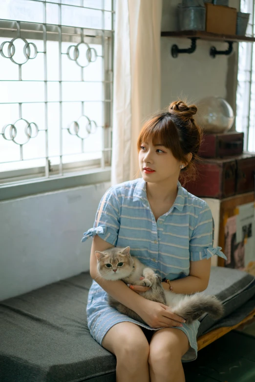 a woman holding a little cat by some windows