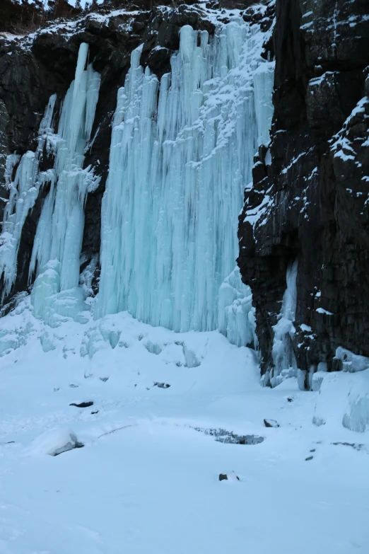two people ski by large icicles on the side of a mountain