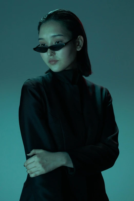 a woman in black with sunglasses stands against a green background