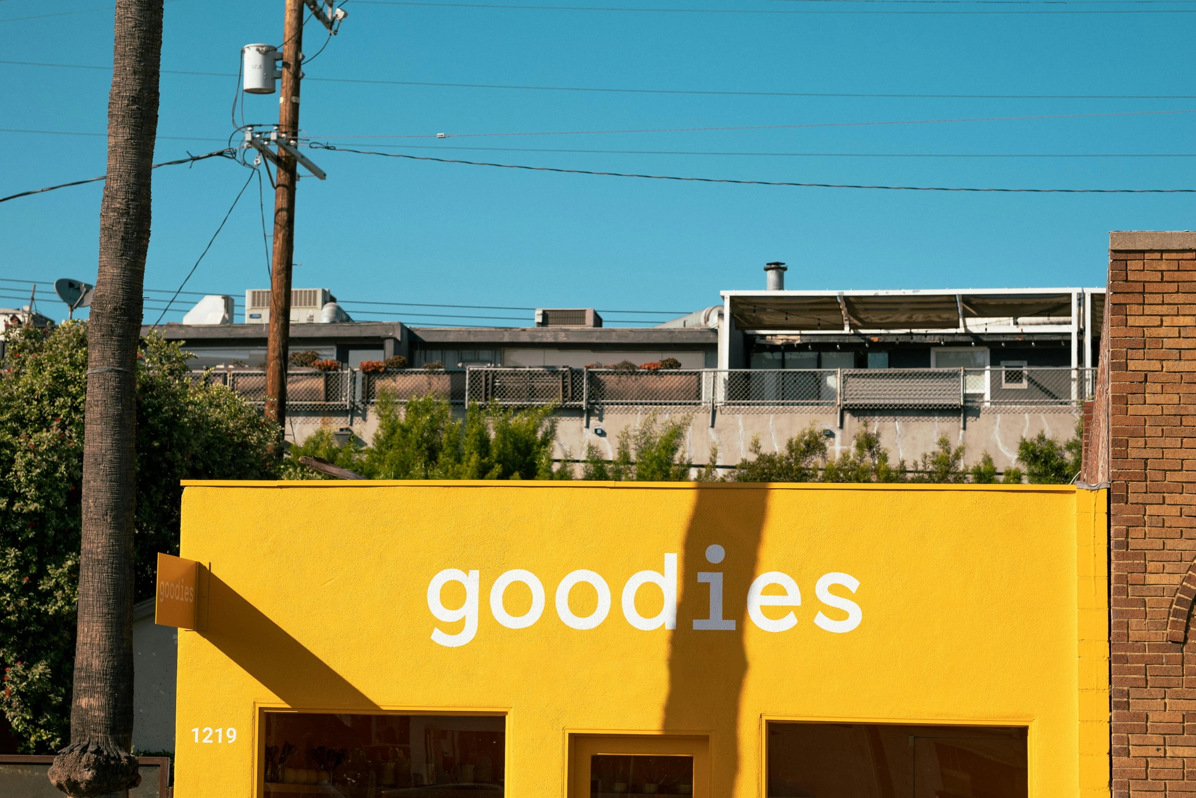 a yellow building on a street corner with a goodies sign in front