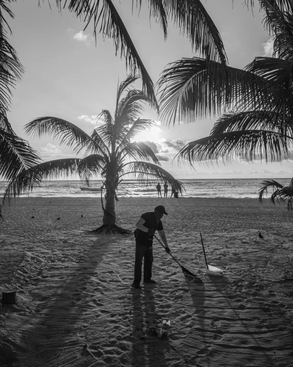 a person sweeping sand on the beach with trees in the background