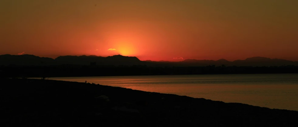 a sunset with a large body of water and mountain range in the distance