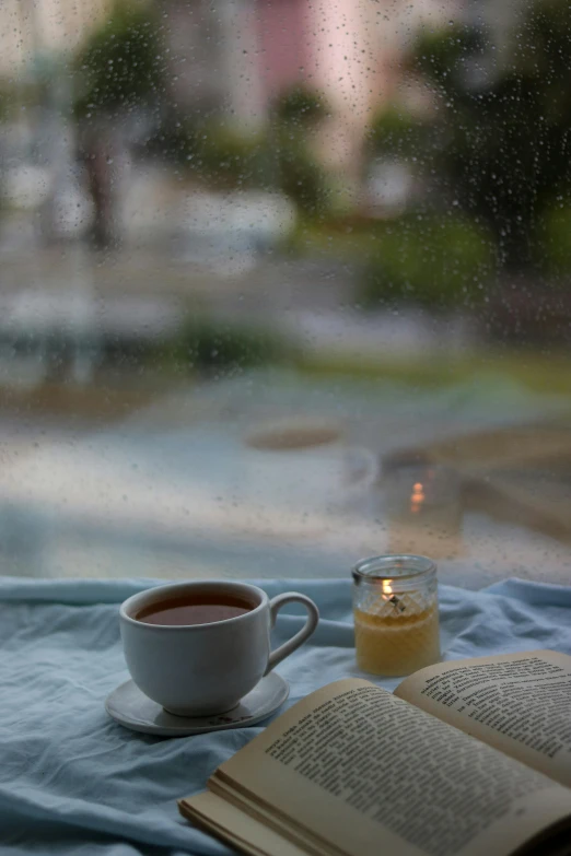 a coffee cup sits on the window sill by a candle and open book