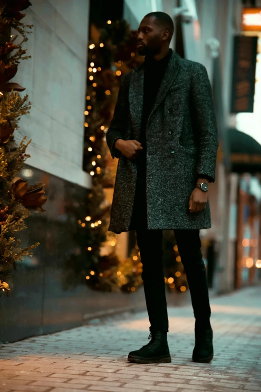 a person wearing black pants, a green and black coat and black boots and a christmas tree