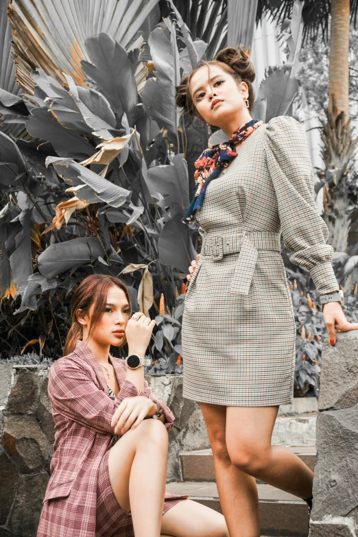 two women are posing for the camera in front of a tree