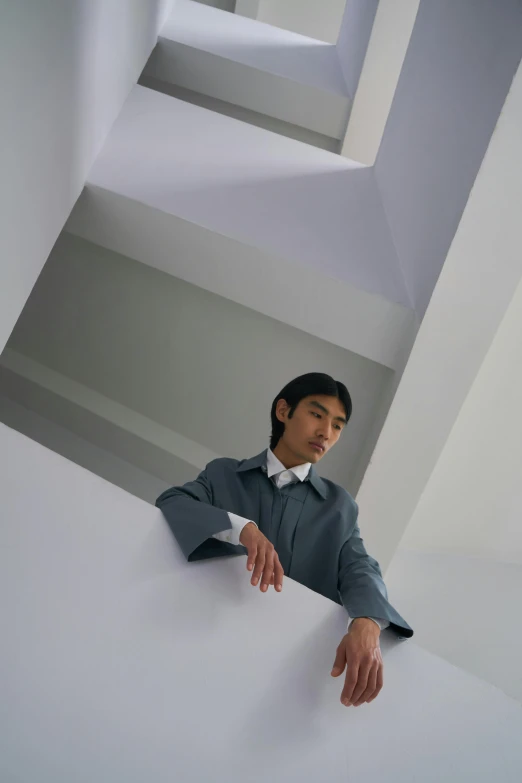 a man with an elegant suit leaning on a white wall