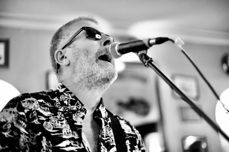 a man in sunglasses and a neck tie singing into a microphone