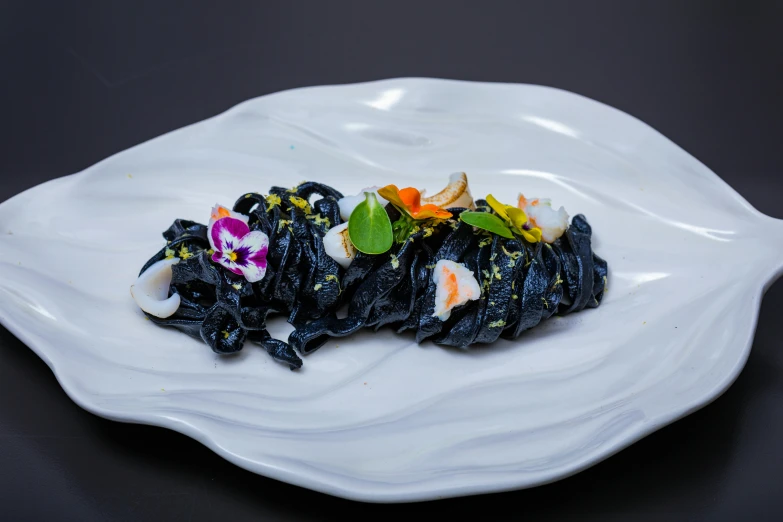 an ornate white plate holds black noodles and flowers