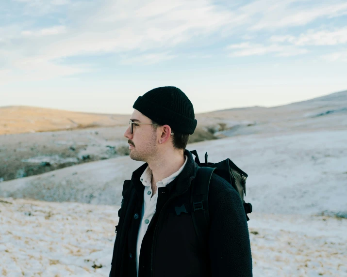 a man is wearing a beanie while he looks out on the snow covered hills