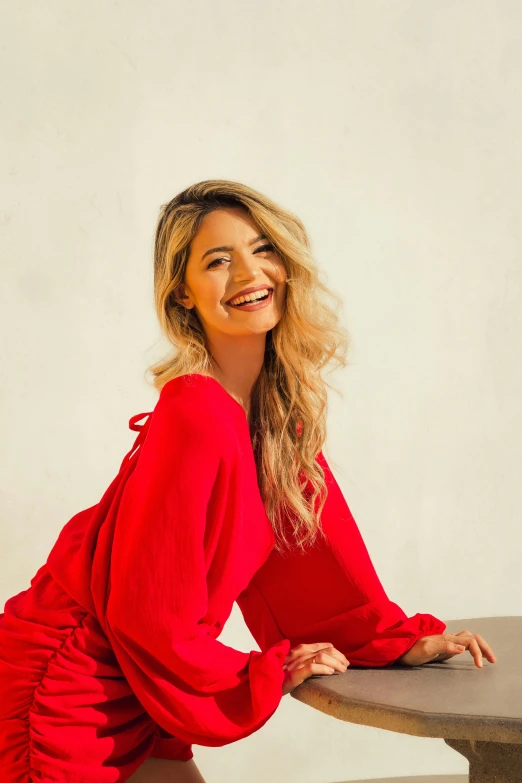 a woman in a red top and blue jeans sitting at a table