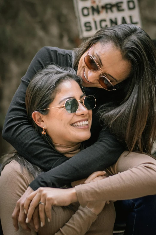 two smiling women hugging and leaning against a pole