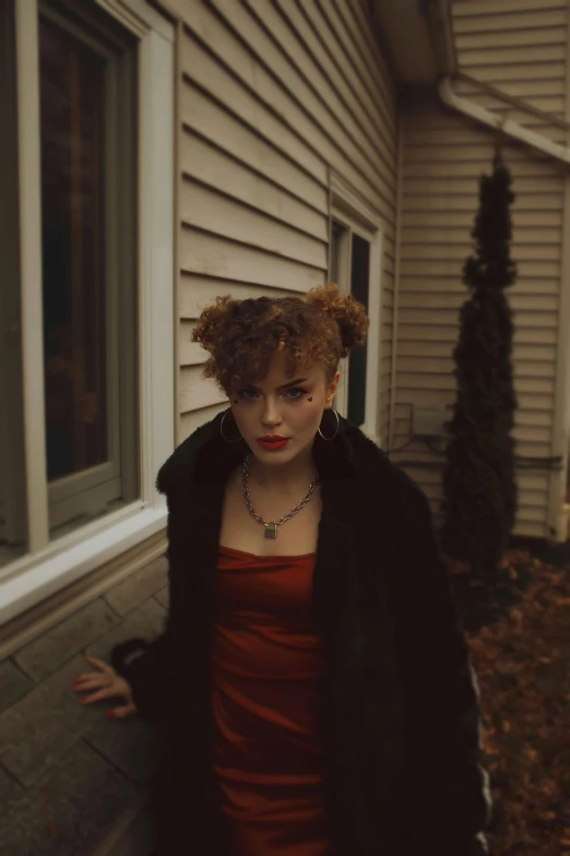 a woman standing outside a house wearing a black coat