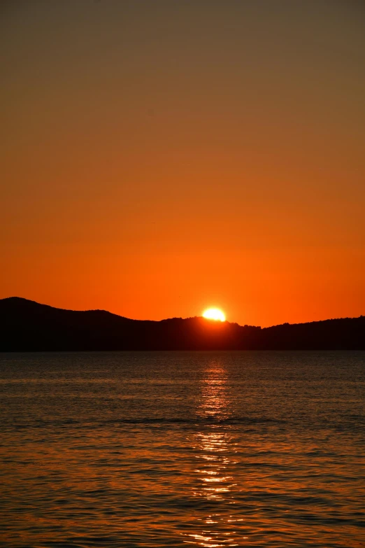 a sunset over the water with mountains in the distance