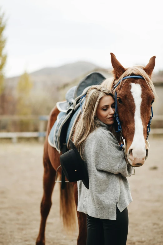 a woman stands next to a brown and white horse