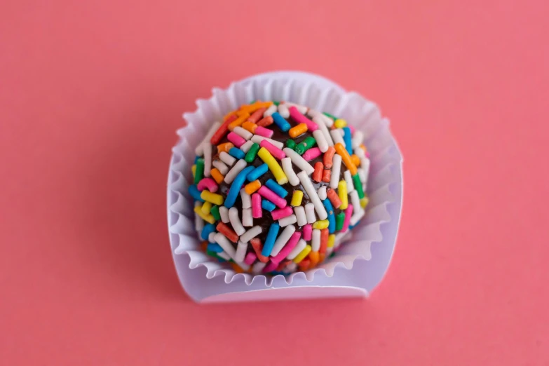 an assortment of sprinkles in a white bowl on a pink background