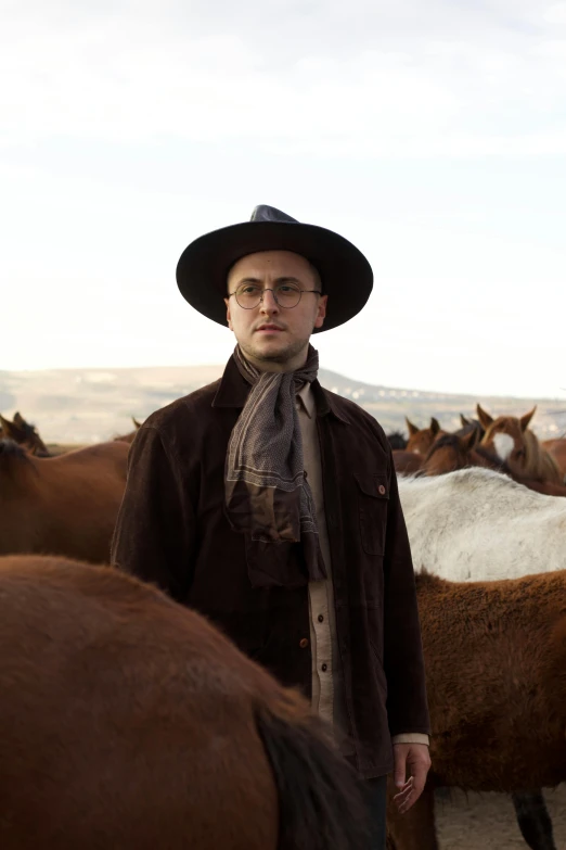 a man wearing a cowboy hat and eye glasses near a bunch of brown and white horses