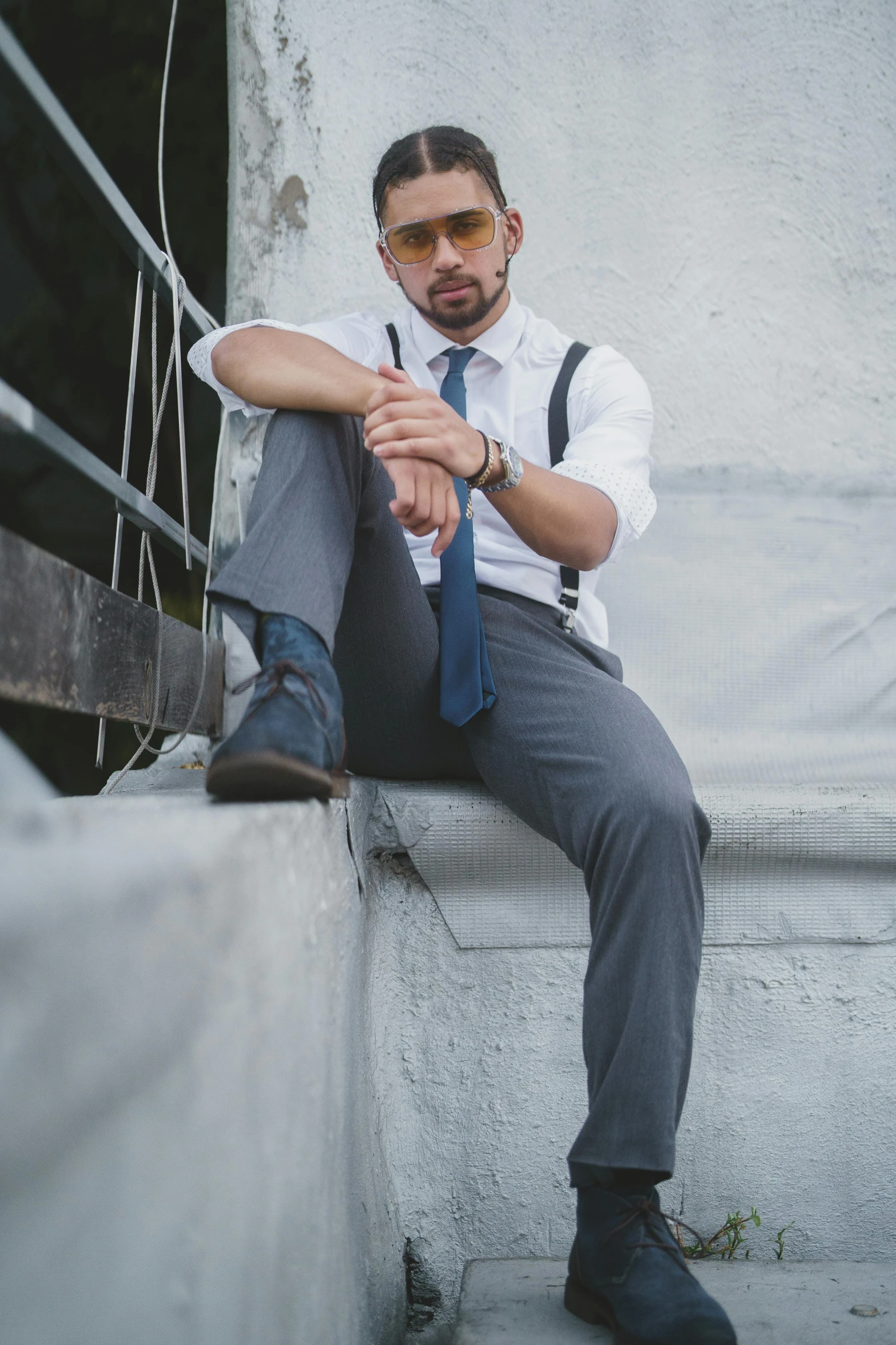 man with long hair and glasses sitting next to cement building