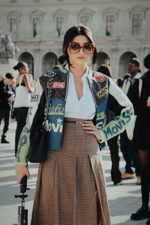 a woman with sunglasses and a jacket on stands near a building