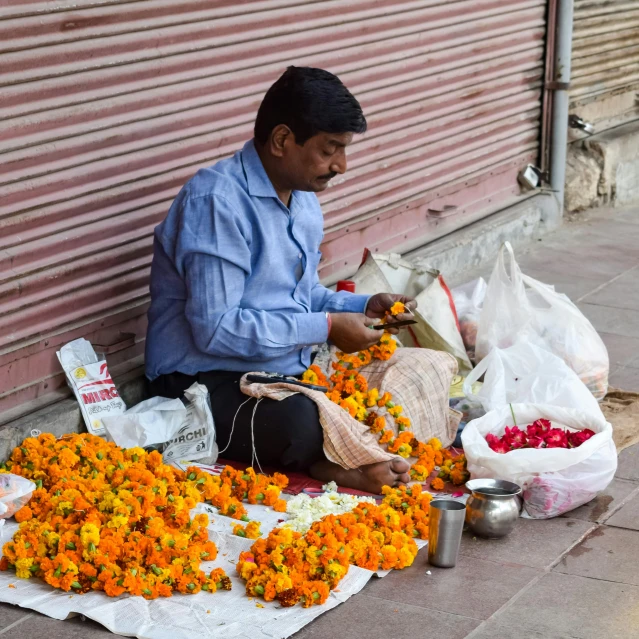 a man sits on the side of a building selling flowers