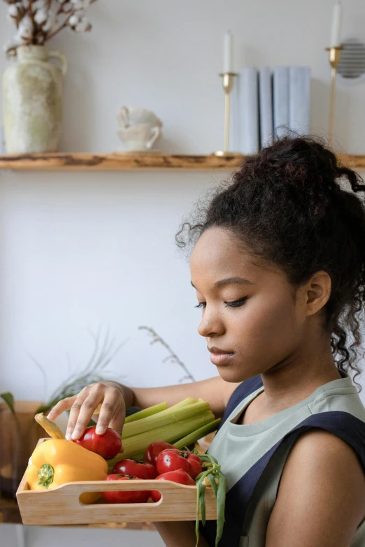 a young woman sitting down and holding a wooden box filled with vegetables