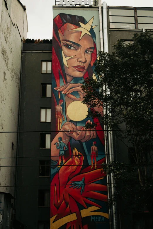 a mural on a wall of a woman holding a medallion in front of a building with trees