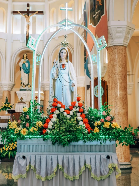 the statue of a virgin stands in a small church with flower decoration