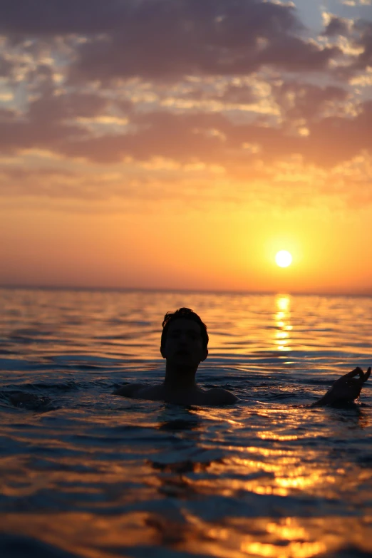 the man is swimming in the water at sunset