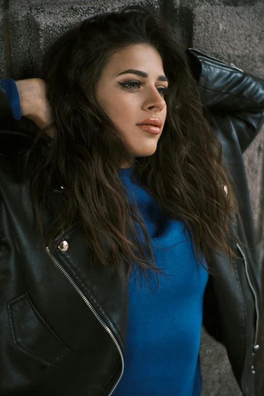 a woman in blue and a black jacket leaning up against a wall
