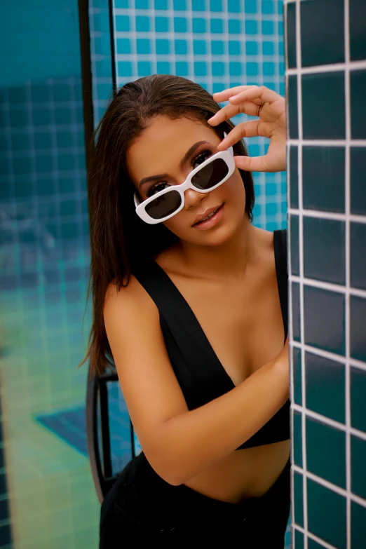 a woman in a bathing suit and sunglasses standing near a wall