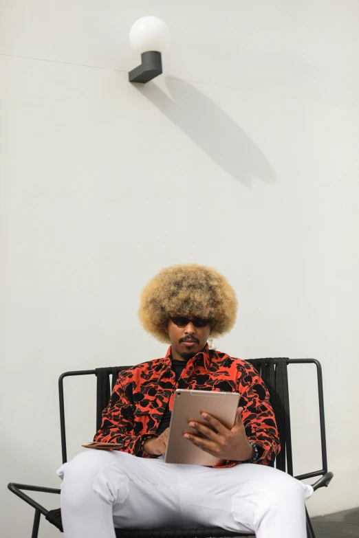 man with afro hair using a tablet on a chair
