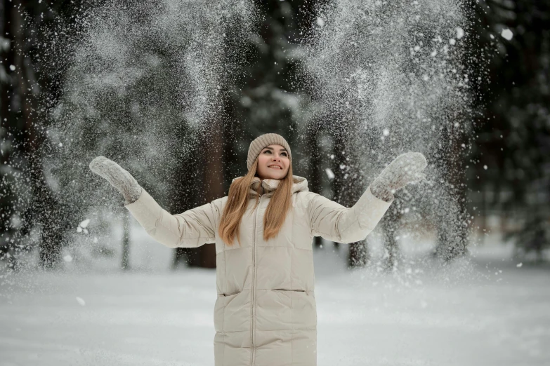 a woman standing in a snowy forest, arms spread out and throwing snow