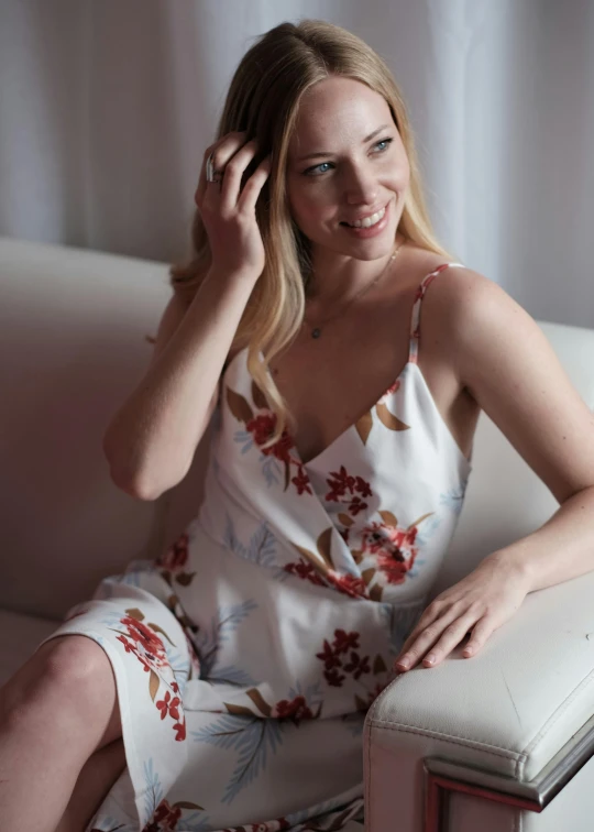 a woman sits on a sofa smiling wearing a dress