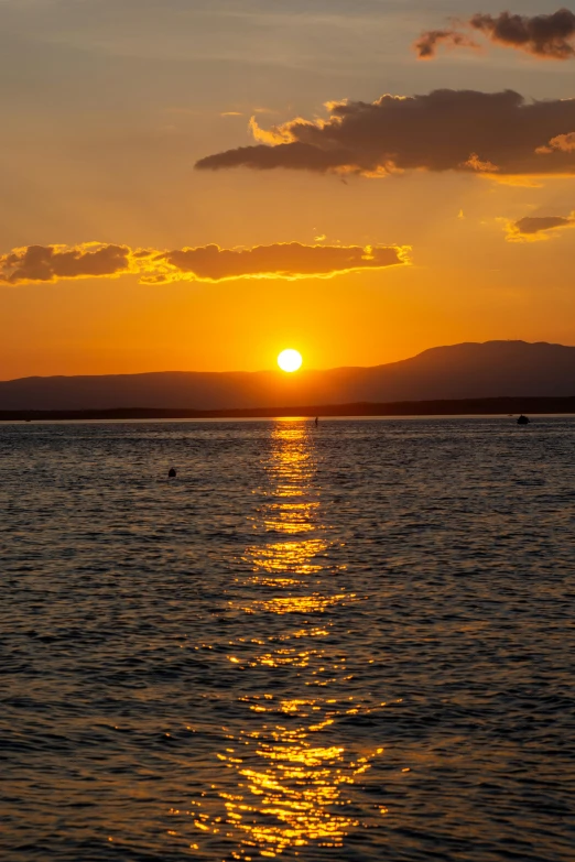 the sun is setting over the water with a few clouds