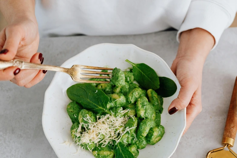 a woman is holding a fork while putting some green food into her bowl