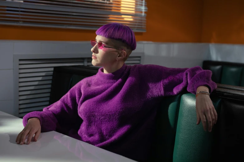 an older lady wearing a pink sweater and purple pants sits at a table