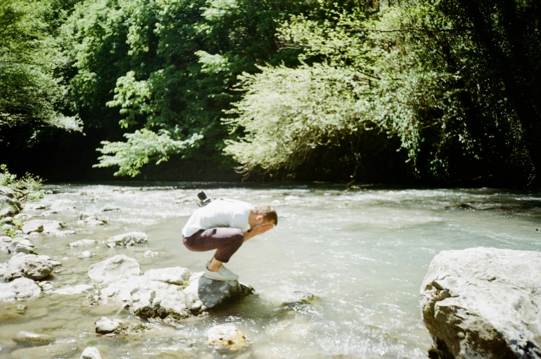 a man is kneeling down on rocks by a creek