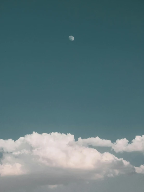 a jet in the sky with clouds and a moon in the sky