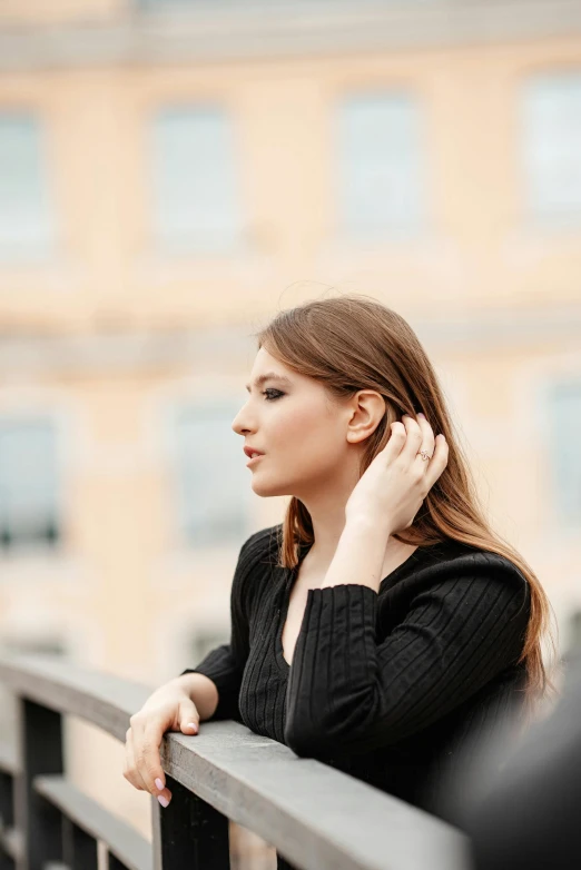 a woman leaning against a railing, holding her hand behind her head