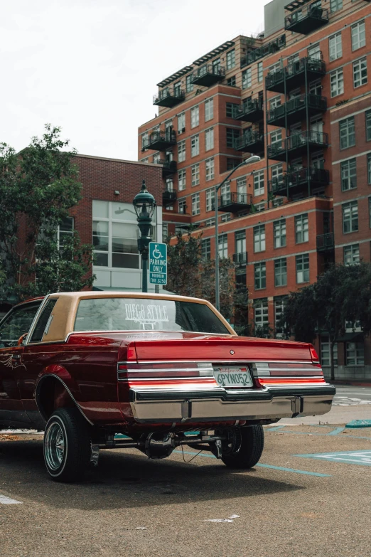 an antique maroon car is parked in front of tall buildings