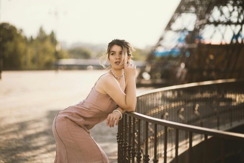 a woman in pink dress leaning against a fence with a cell phone