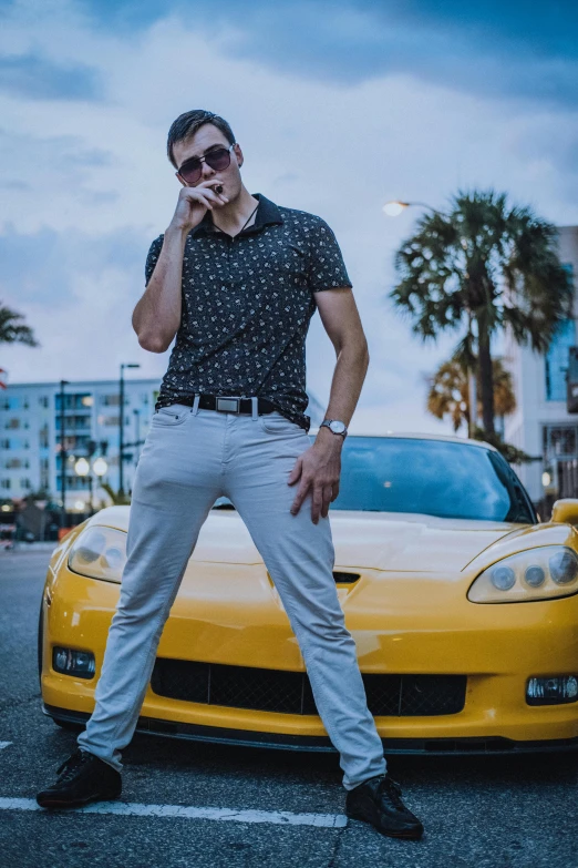 the man is leaning on the car's tire to speak on the phone