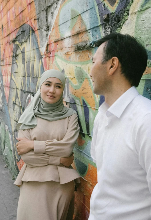 a man and woman standing together in front of graffiti covered wall